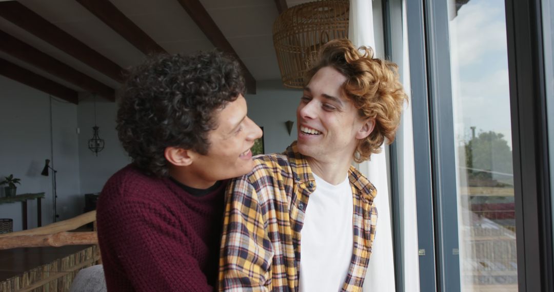 Happy Diverse LGBTQ Couple Embracing by Window at Home