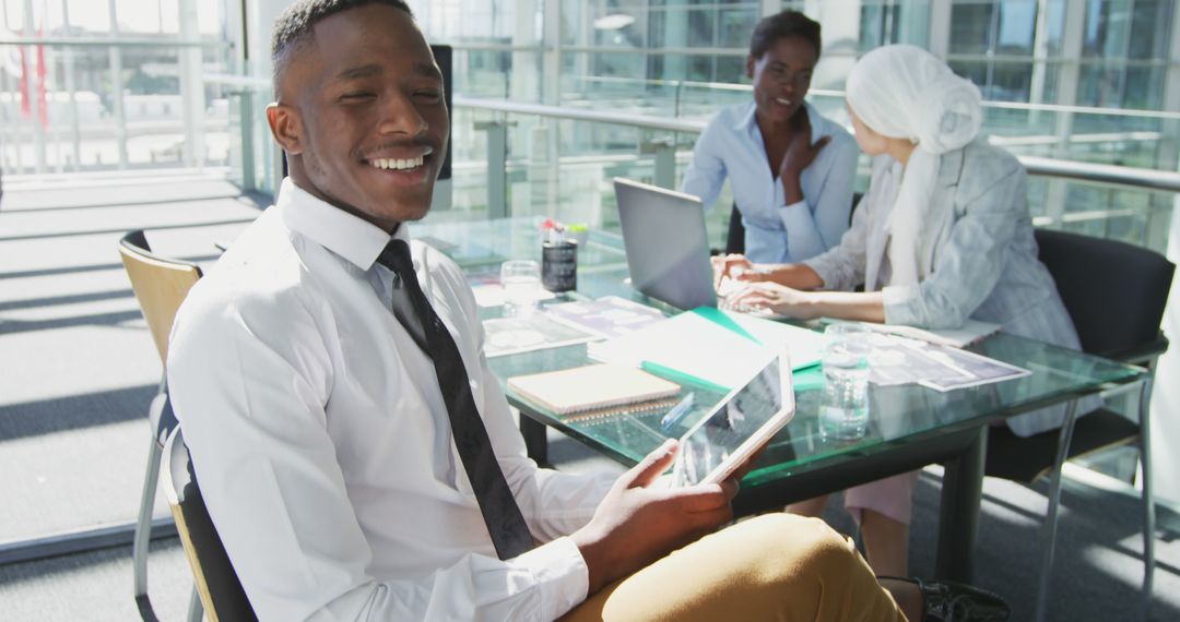 Smiling Businessman Holding Tablet in Office with Colleagues Working in Background - Free Images, Stock Photos and Pictures on Pikwizard.com