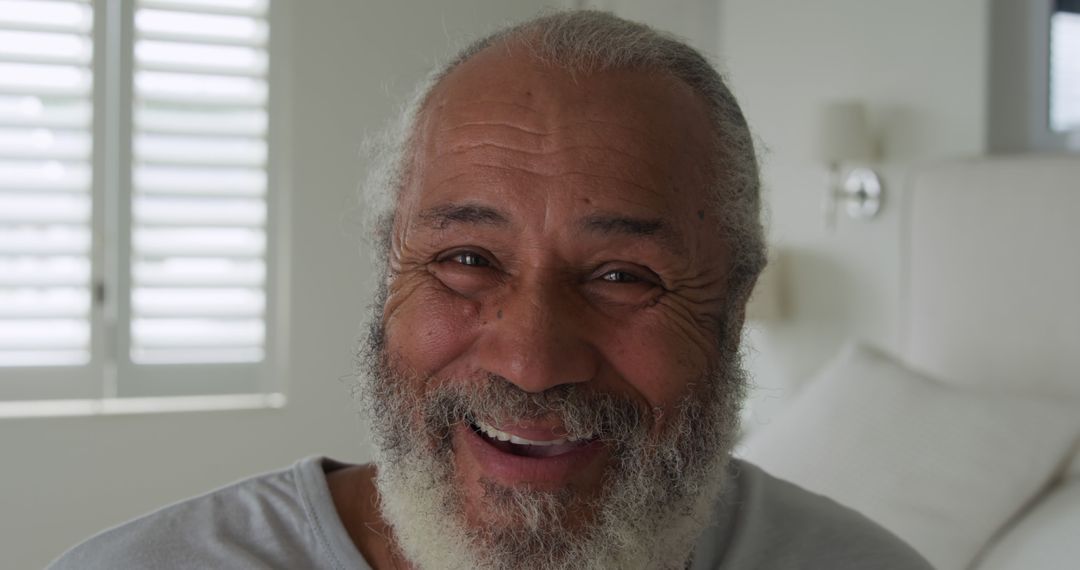 Elderly man with warm smile and beard sitting indoors - Free Images, Stock Photos and Pictures on Pikwizard.com