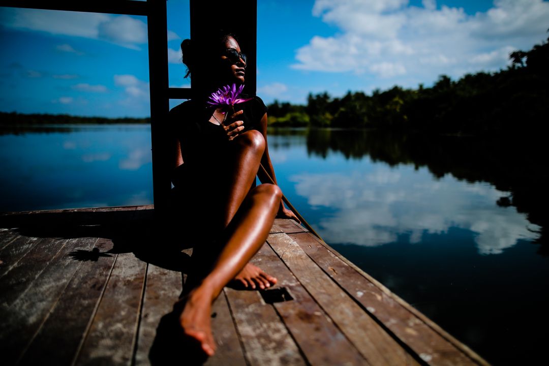 Relaxed Woman Holding Purple Flower Relaxing on Dock by Tranquil Lake - Free Images, Stock Photos and Pictures on Pikwizard.com