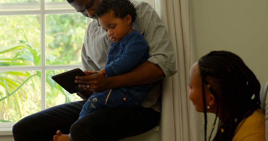 Father and Child Using Tablet by Window, Mother Smiling - Free Images, Stock Photos and Pictures on Pikwizard.com