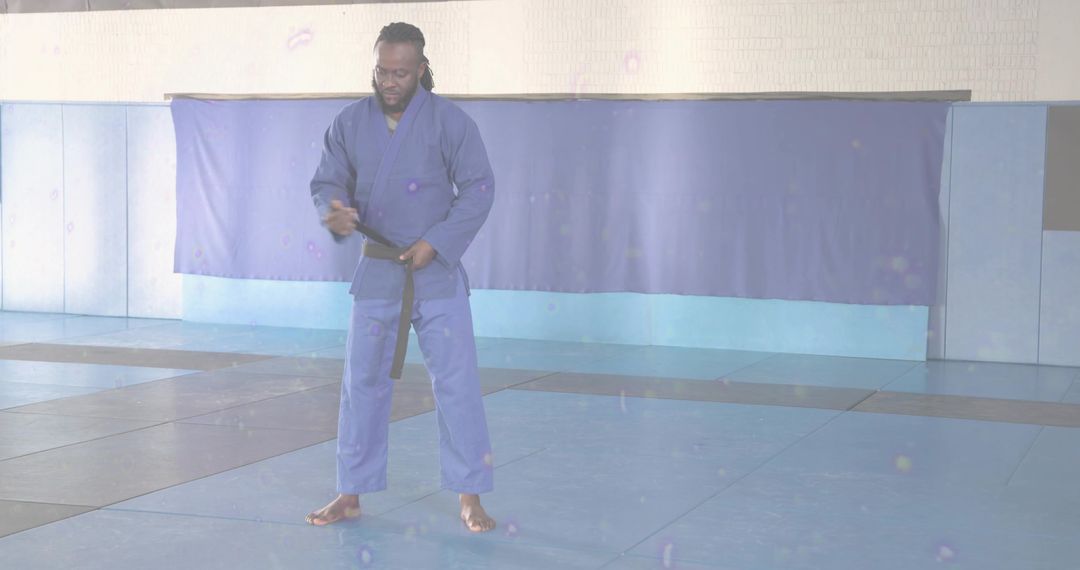 Martial artist adjusting black belt in dojo wearing blue gi and training on mats