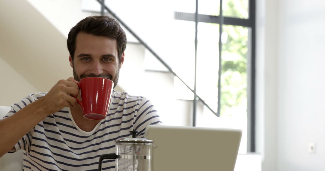 Smiling Man Drinking Coffee While Working on Laptop at Home - Free Images, Stock Photos and Pictures on Pikwizard.com