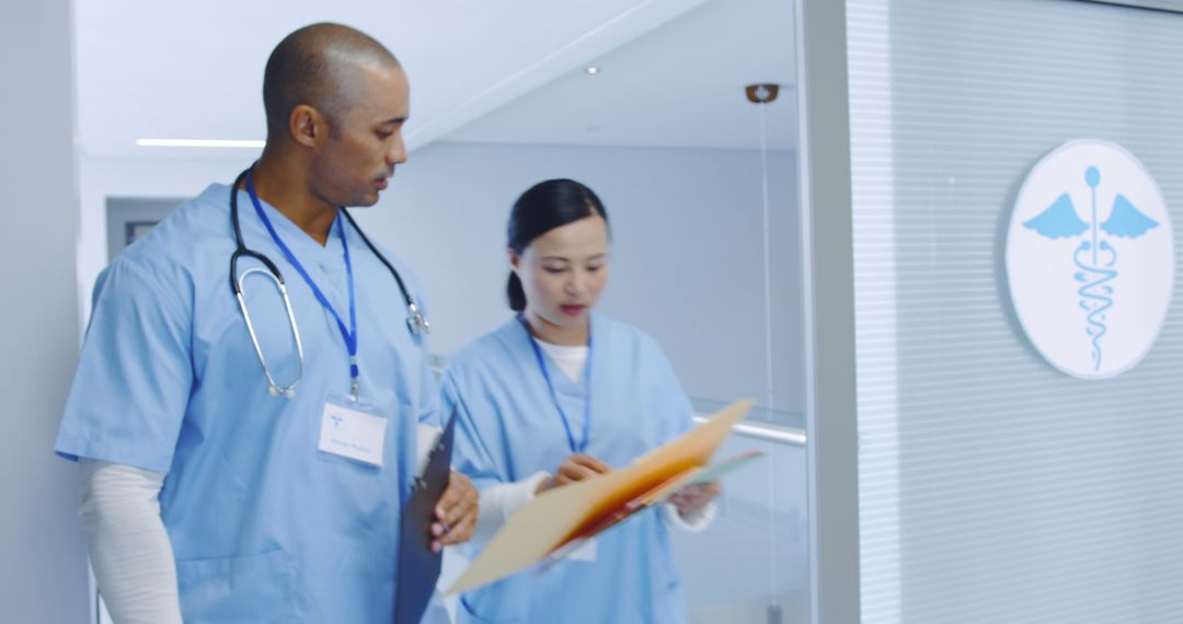 Two Diverse Healthcare Professionals Discussing Patient Files in Modern Hospital Corridor - Free Images, Stock Photos and Pictures on Pikwizard.com