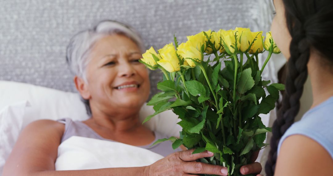 A girl gives yellow roses to a happy elderly woman in bed, symbolizing intergenerational love. - Free Images, Stock Photos and Pictures on Pikwizard.com