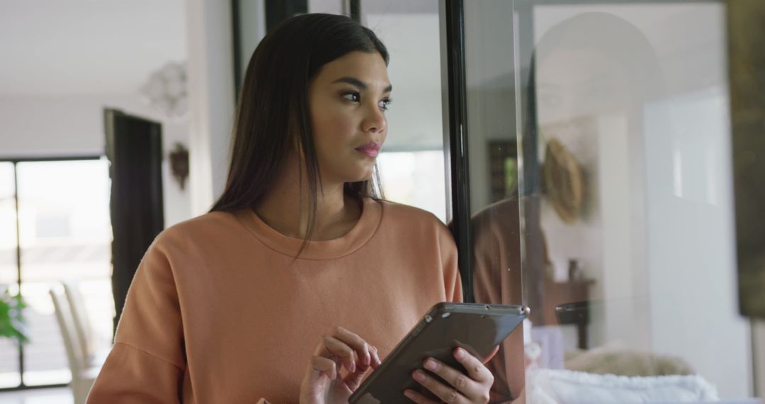 Image of thoughtful biracial woman standing at window and using tablet - Free Images, Stock Photos and Pictures on Pikwizard.com