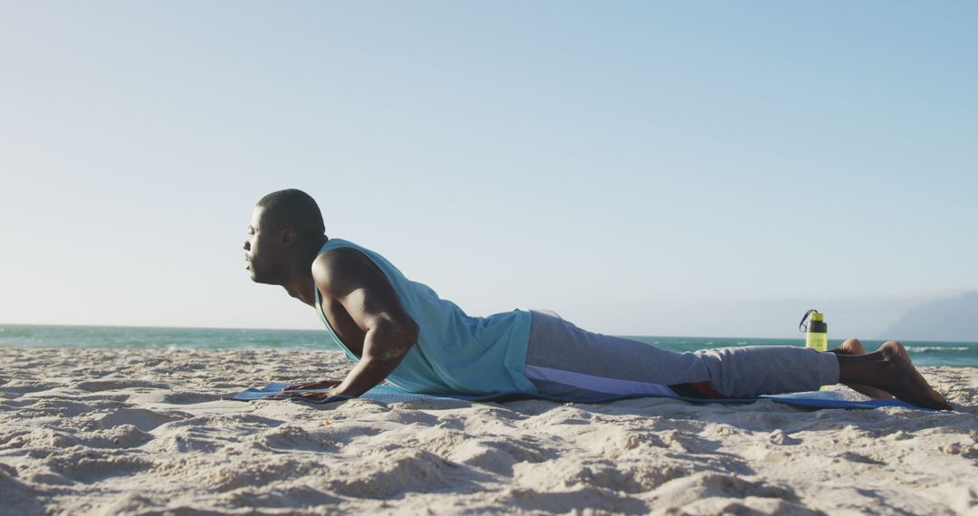Focused african american man practicing yoga on beach, exercising outdoors by the sea - Free Images, Stock Photos and Pictures on Pikwizard.com