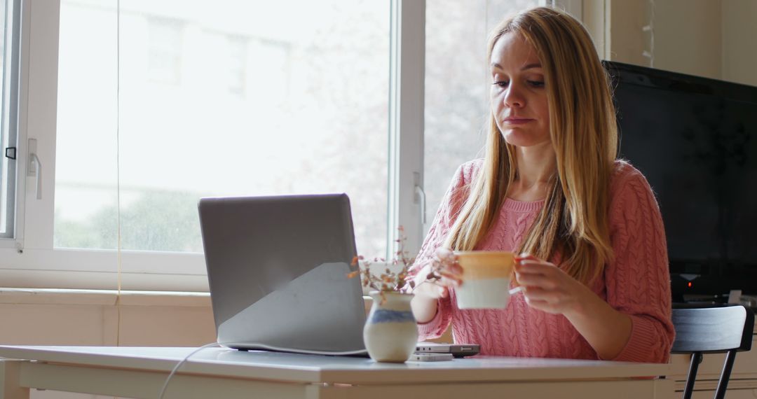 Woman Working on Laptop Holding Coffee in Bright Home Office - Free Images, Stock Photos and Pictures on Pikwizard.com