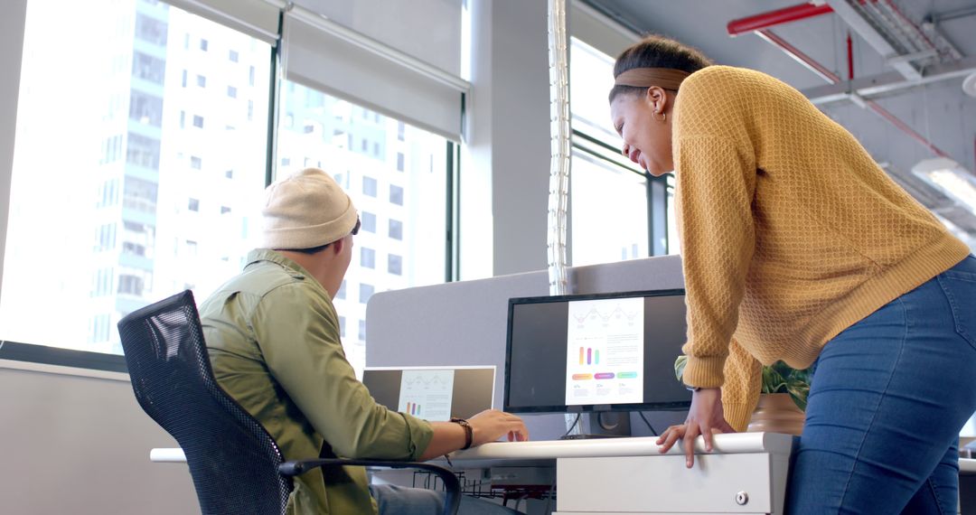 Diverse coworkers collaborating and reviewing analytics on laptop and monitor in office