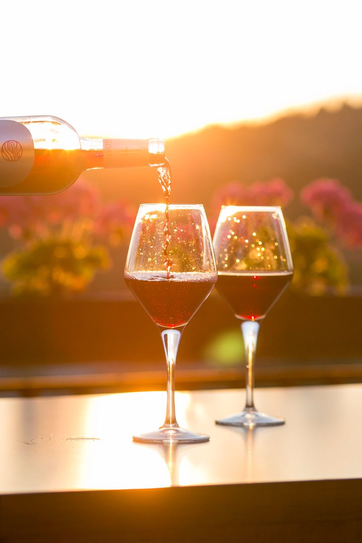 Sunset pouring red wine into glasses on outdoor table with bokeh flowers