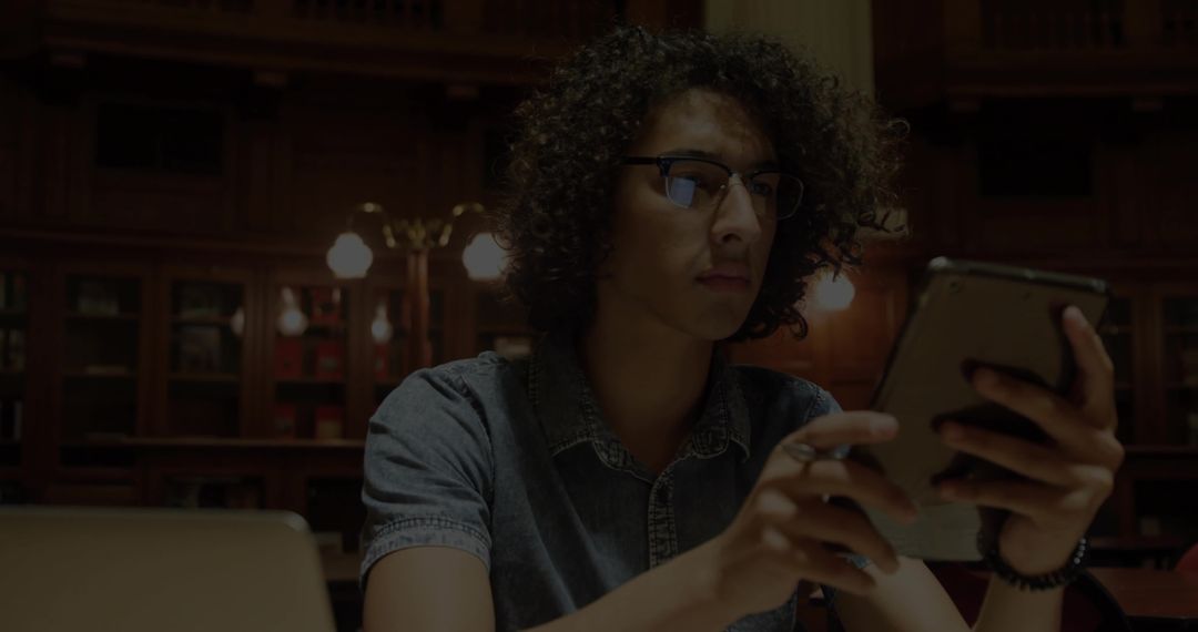 Curly Haired Man Engaged with Tablet in Classic Library Ambience