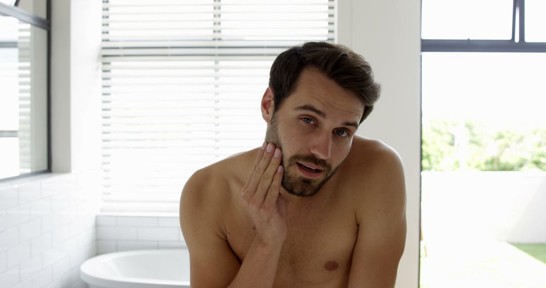 Young Caucasian Man Examining Face in Bathroom Focused on Skincare - Free Images, Stock Photos and Pictures on Pikwizard.com