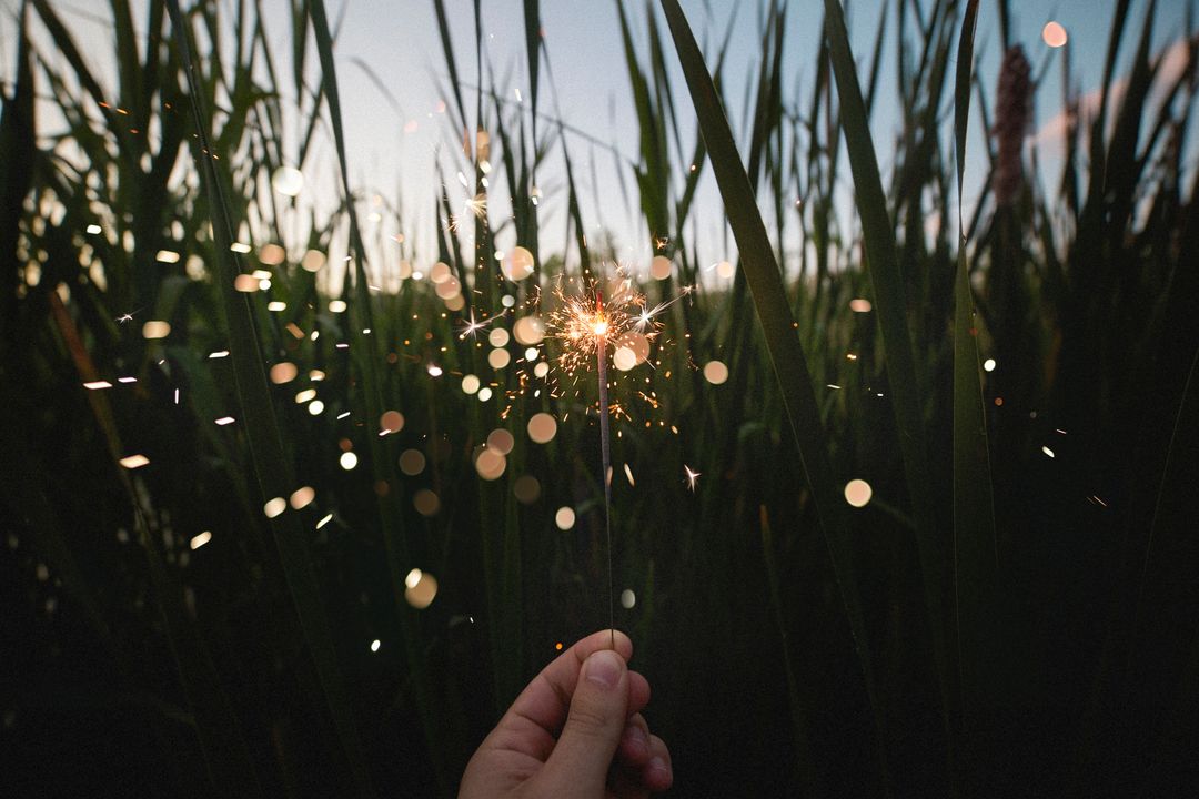Hand Holding Sparkler in Grassy Field at Twilight
