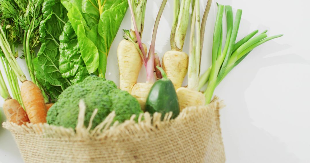 Burlap sack holding fresh organic vegetables in minimal flat lay on white surface, rustic produce