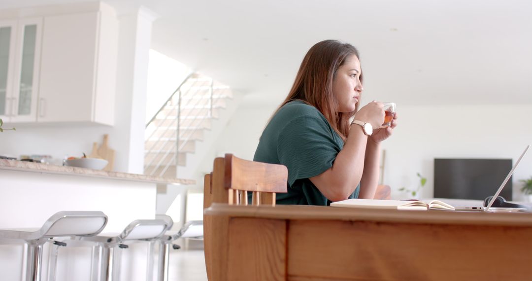 Thoughtful Plus Size Woman Enjoying Tea and Working on Laptop at Home