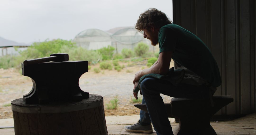 Man Contemplating While Sitting on Anvil in Workshop - Free Images, Stock Photos and Pictures on Pikwizard.com