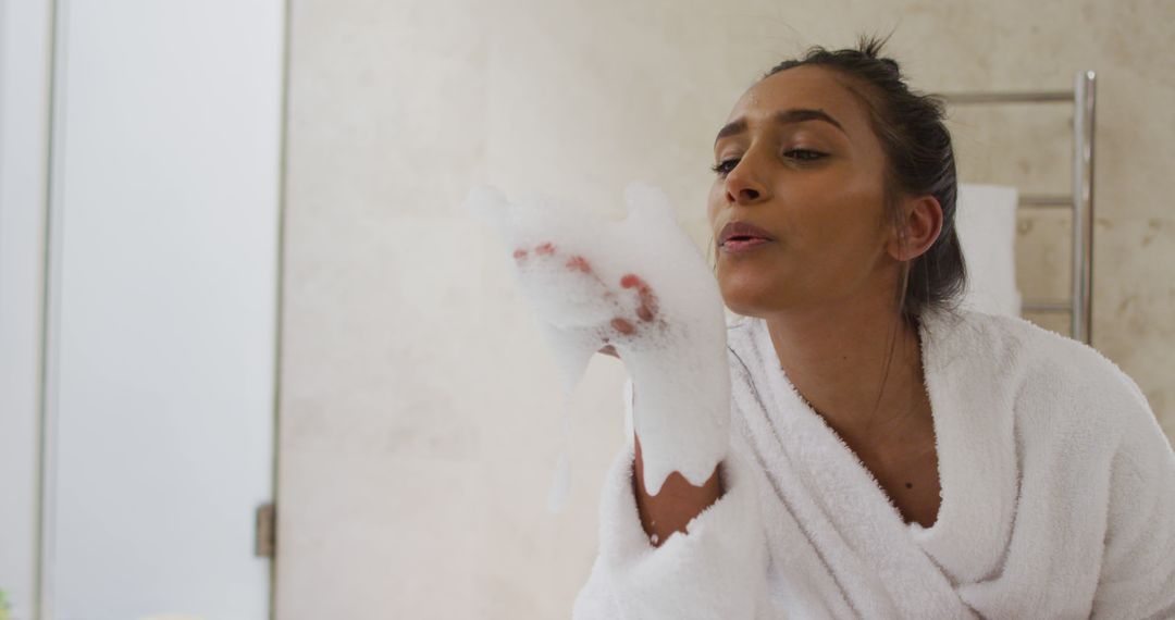 Relaxed Woman in Bathrobe Blowing Foam Bubbles in Bathroom - Free Images, Stock Photos and Pictures on Pikwizard.com