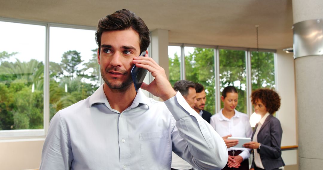 Confident Businessman Talking on Phone in Modern Office with Colleagues Collaborating - Free Images, Stock Photos and Pictures on Pikwizard.com