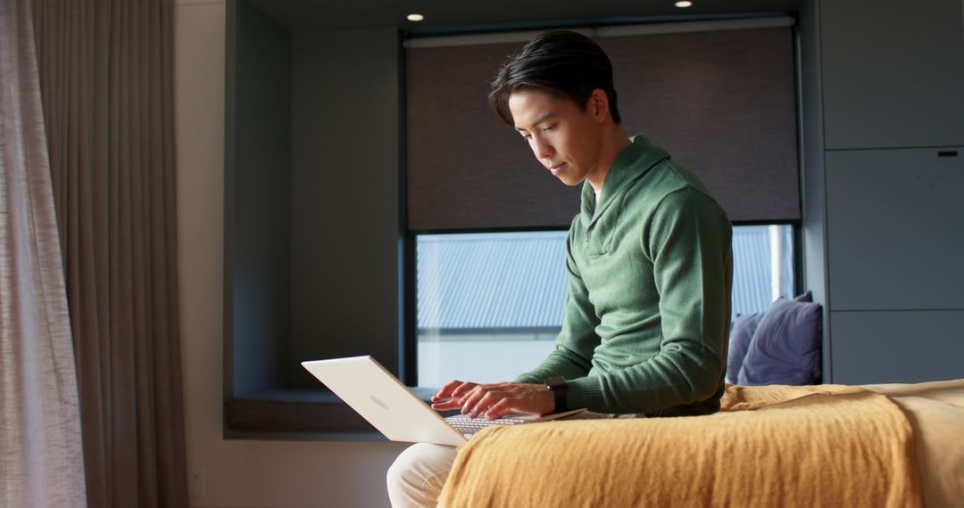 Young Man Relaxing While Working on Laptop in Cozy Bedroom