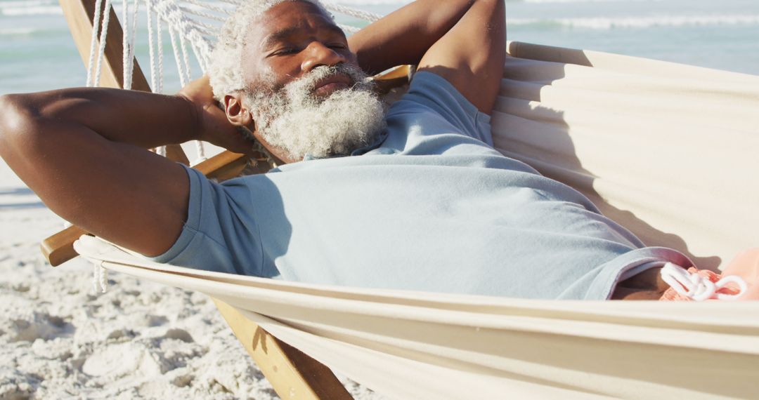 Happy senior african american man lying in hammock on sunny beach - Free Images, Stock Photos and Pictures on Pikwizard.com