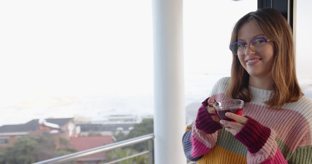 Woman Relaxing on Balcony Overlooking Ocean with Warm Drink