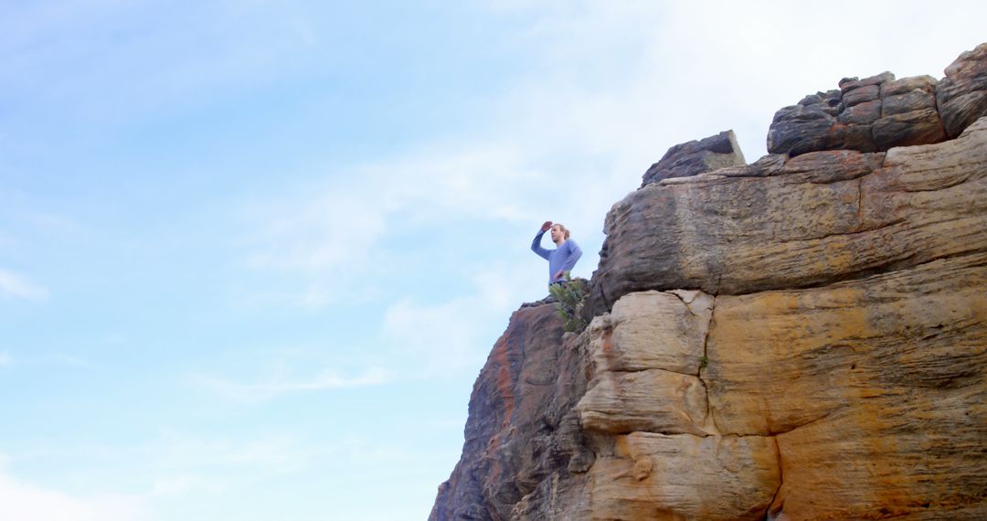 Person Standing on Rocky Cliff Against a Blue Sky - Free Images, Stock Photos and Pictures on Pikwizard.com