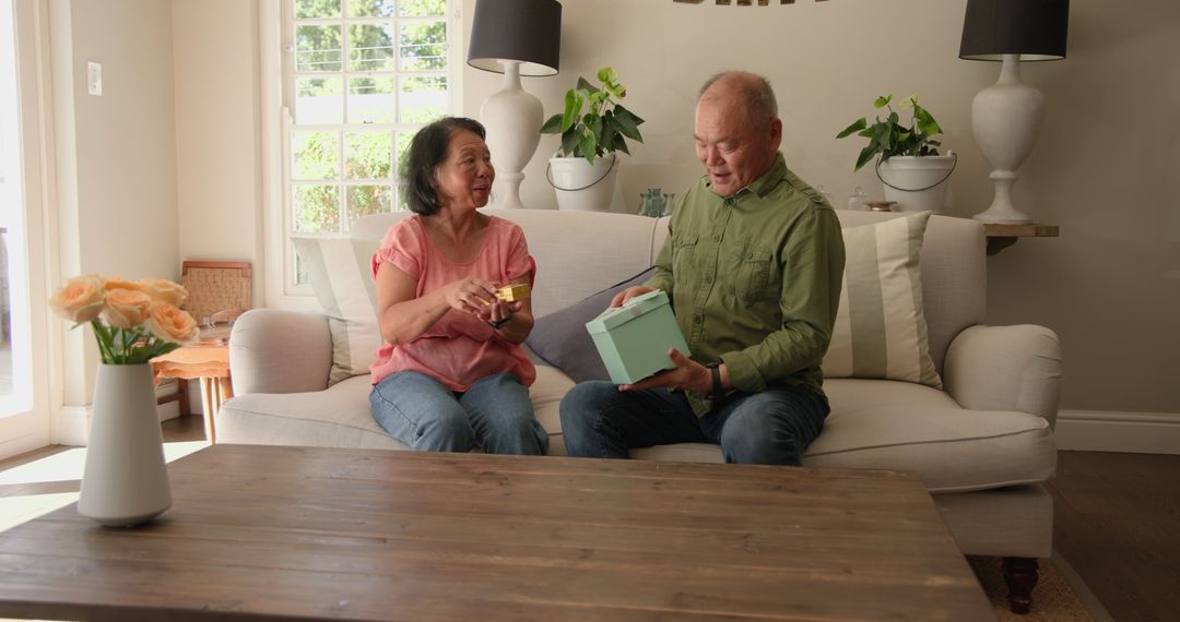 Senior Couple Smiling While Unwrapping Gift Together on Couch