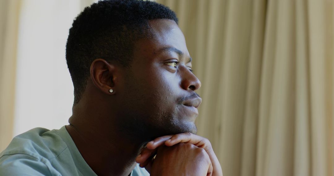 Pensive man gazing out window resting chin on hands wearing stud earring