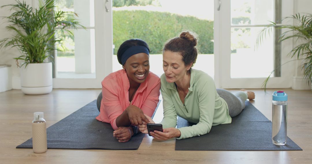 Diverse Friends Relaxing Together on Yoga Mats While Using Smartphone