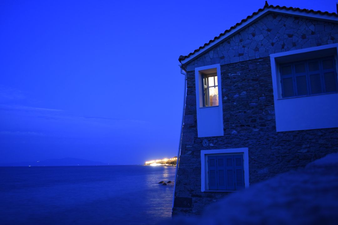 Cozy seaside house at night with warm interior light shining from window - Free Images, Stock Photos and Pictures on Pikwizard.com