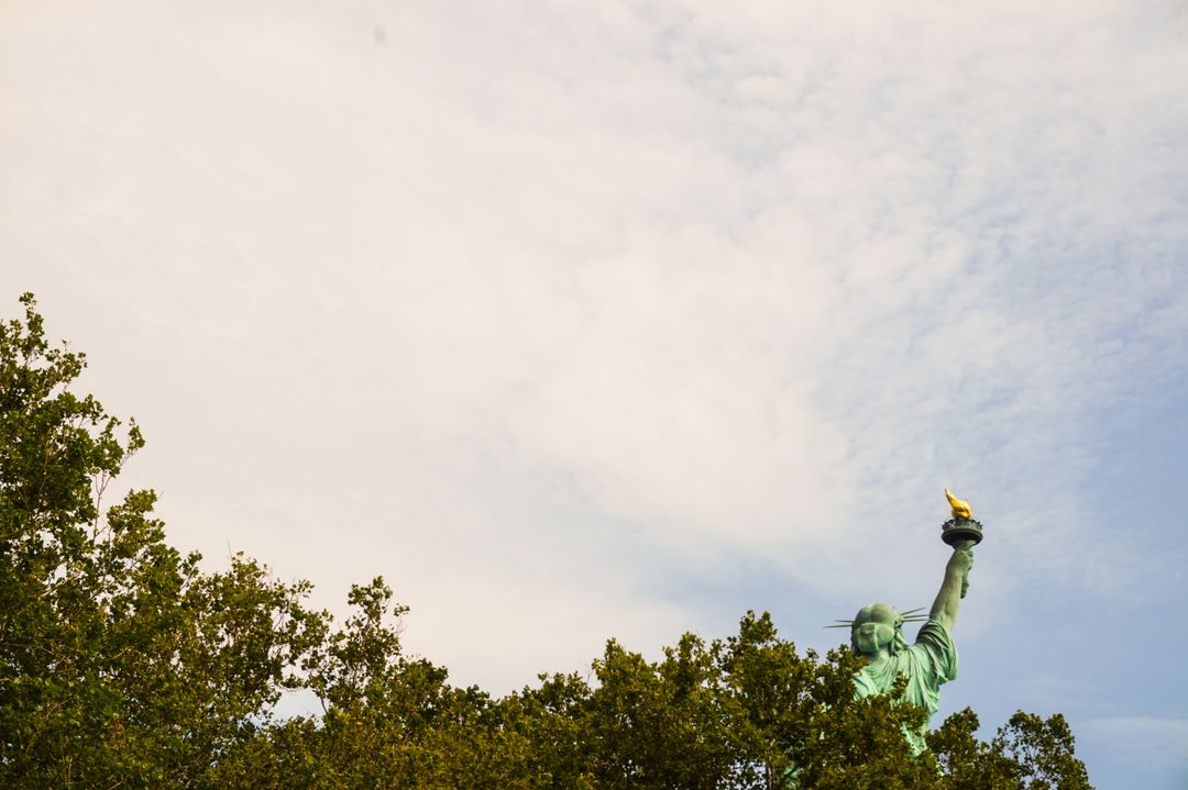 Statue of Liberty Torch Above Green Trees Against Sky