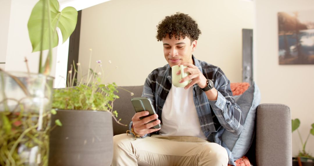 Young Man Relaxing at Home Drinking Coffee While Using Smartphone - Free Images, Stock Photos and Pictures on Pikwizard.com