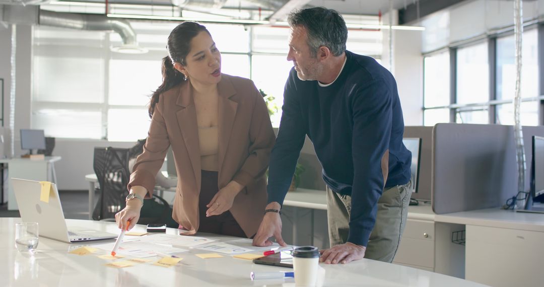 Two colleagues collaborating over sticky notes and laptop in modern open-plan office