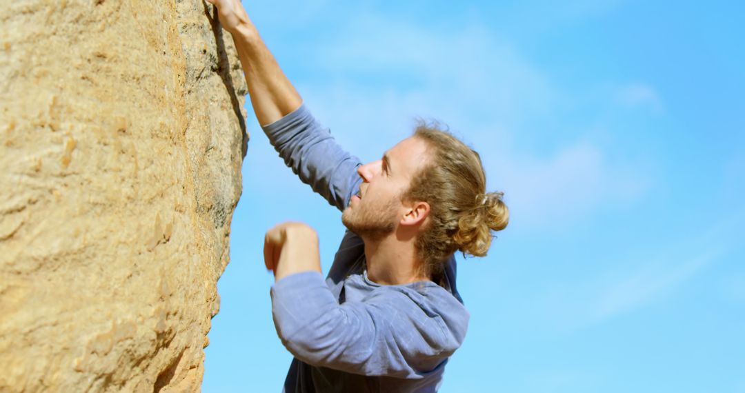 Happy caucasian male rock climber with long hair climbing rock face ...