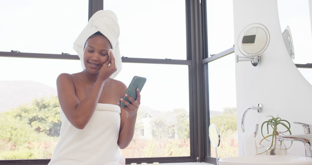 Smiling Woman in Towel Using Smartphone Near Bathroom Window - Free Images, Stock Photos and Pictures on Pikwizard.com