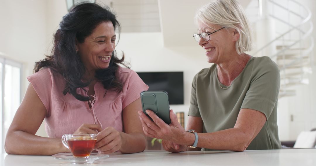 Friendly Senior Women Sharing a Laugh with Smartphone over Tea - Free Images, Stock Photos and Pictures on Pikwizard.com