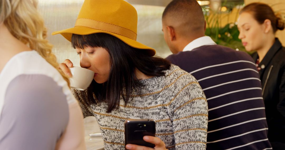 Young Woman in Yellow Hat Drinking Coffee and Using Smartphone in Cafeteria - Free Images, Stock Photos and Pictures on Pikwizard.com