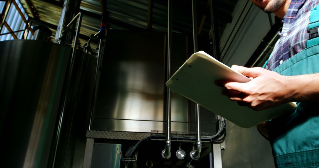 A worker in an industrial setting is monitoring equipment using a tablet, with copy space - Free Images, Stock Photos and Pictures on Pikwizard.com