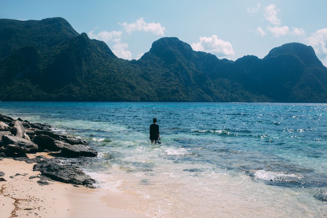 Solitary Person Standing in Shallow Tropical Waters with Mountain Backdrop - Free Images, Stock Photos and Pictures on Pikwizard.com