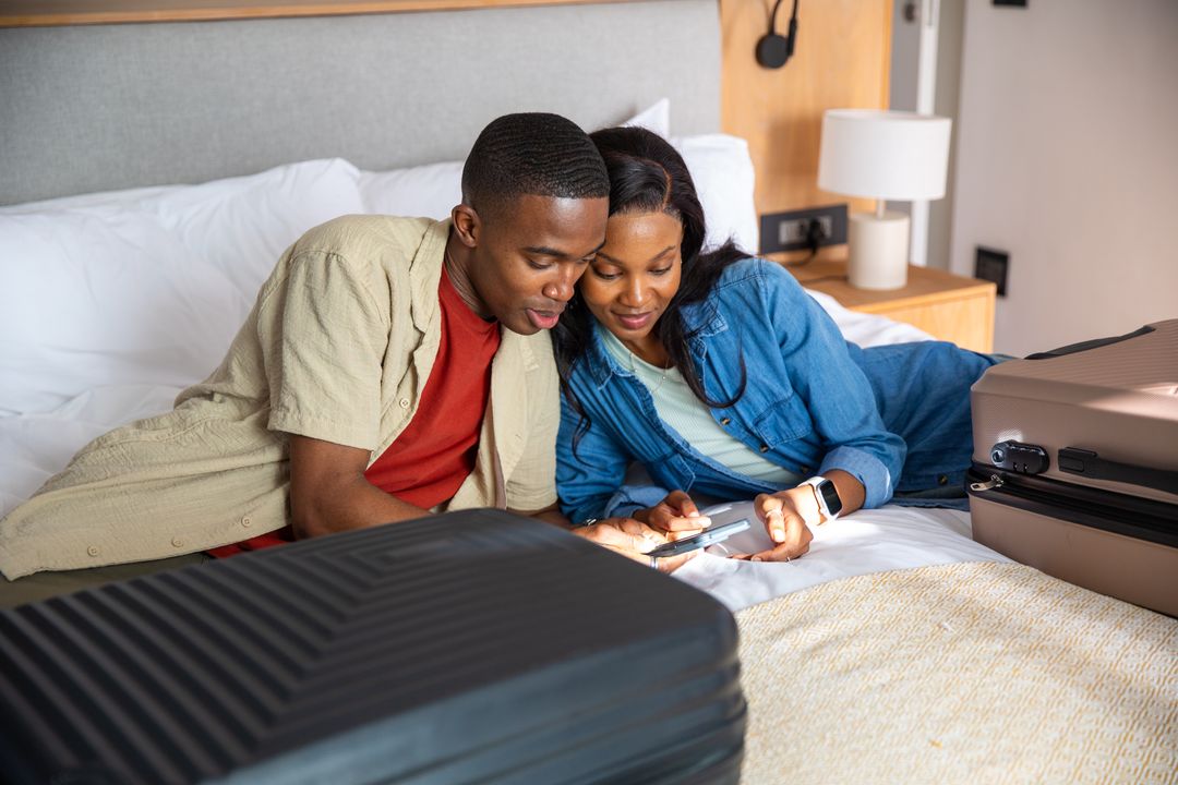 Couple Relaxing with Smartphone on Hotel Bed While Packing