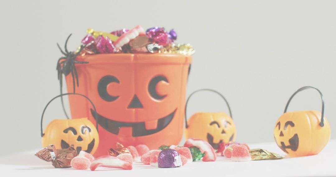 Halloween jack-o-lantern bucket holding assorted candy with mini pumpkin pails and spider