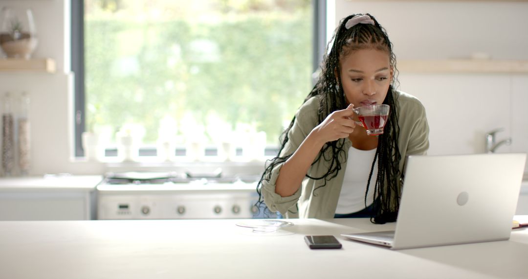 Focused Woman with Braids Drinking Tea while Working on Laptop