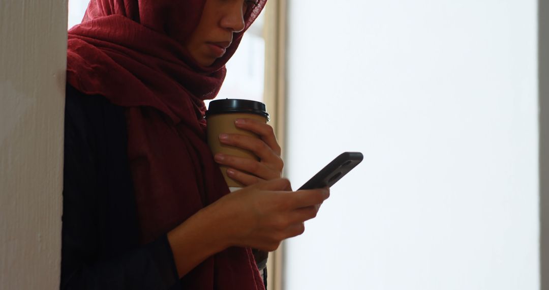 Woman in Hijab Drinking Coffee and Using Smartphone by Window - Free Images, Stock Photos and Pictures on Pikwizard.com