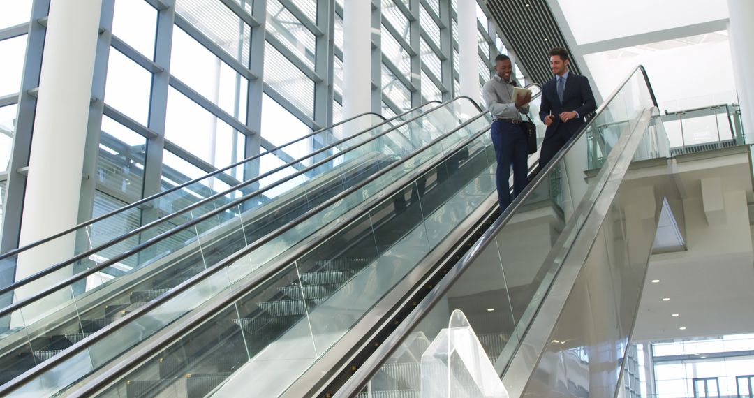 Businessmen discussing work on escalator in modern office building - Free Images, Stock Photos and Pictures on Pikwizard.com