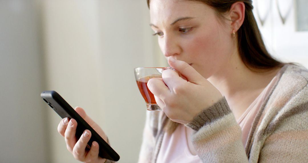 Young Woman Drinking Tea and Using Smartphone in Bright Room - Free Images, Stock Photos and Pictures on Pikwizard.com