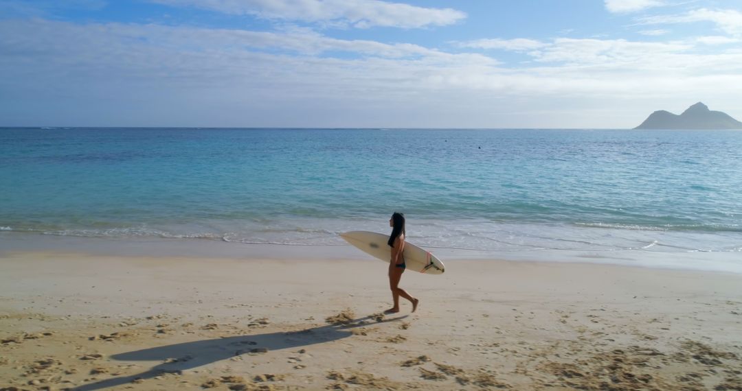 Young biracial woman walks on the beach holding a surfboard - Free Images, Stock Photos and Pictures on Pikwizard.com