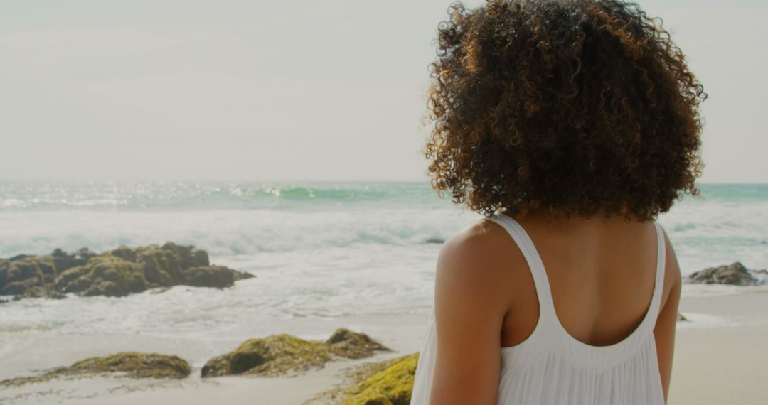 Woman with Curly Hair Enjoying Ocean View on Sunny Beach Day