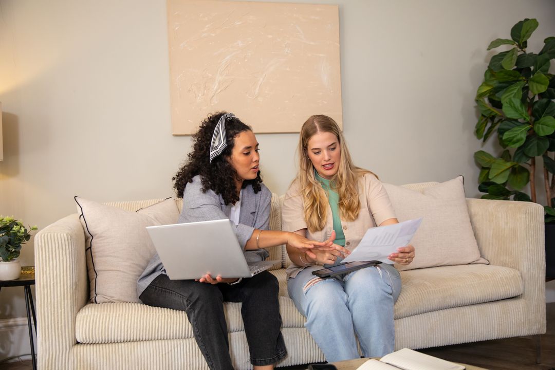 Professional Women Collaborating on Sofa with Laptop and Documents