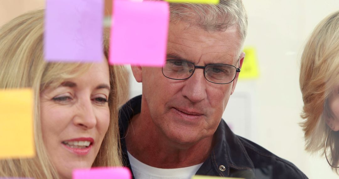Middle-Aged Colleagues Collaborating Through Glass with Sticky Notes