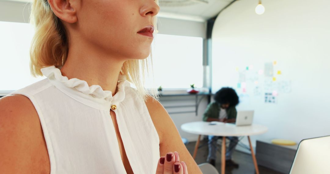 Woman Meditating in Bright Office With Colleague Working in Background - Free Images, Stock Photos and Pictures on Pikwizard.com